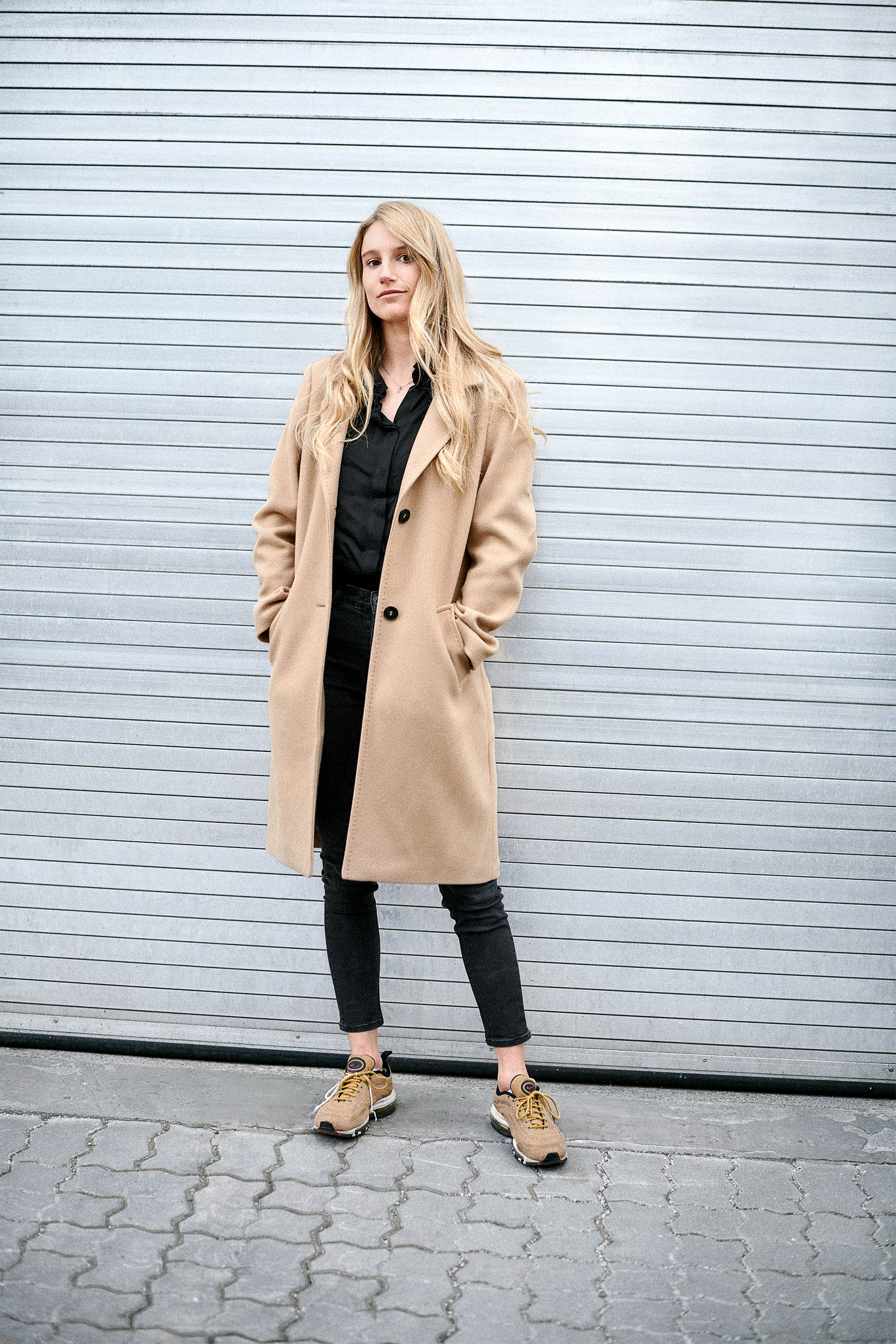 Dressed in a beige coat, Anna Gasser leans against a garage door. 